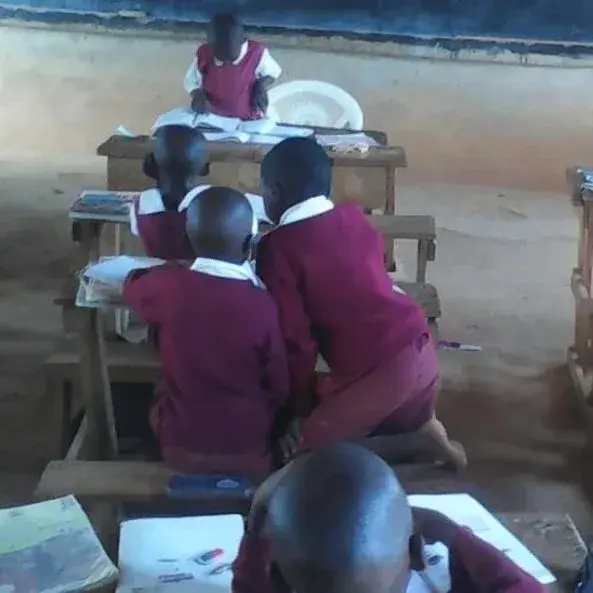Schoolchildren in maroon uniforms share books at a wooden desk