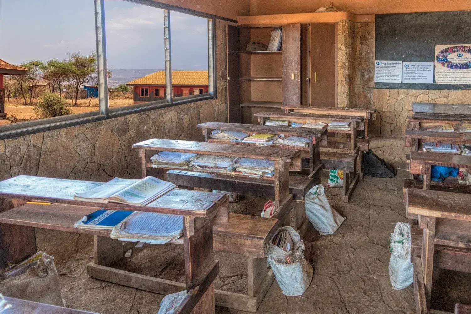 A rural classroom with wooden desks, school bags and open windows looking out to the plain