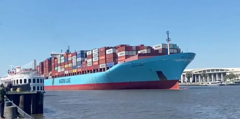 A container ship stacked with shipping containers moored beside a quay under a blue sky