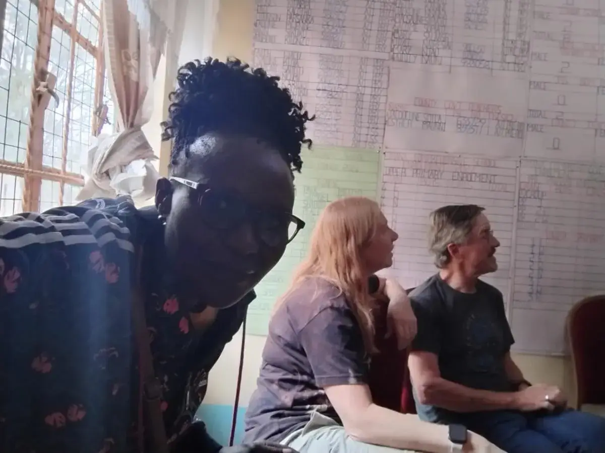 Anna, in glasses, leaning into a selfie in a classroom, with Richard and Greta seated behind her