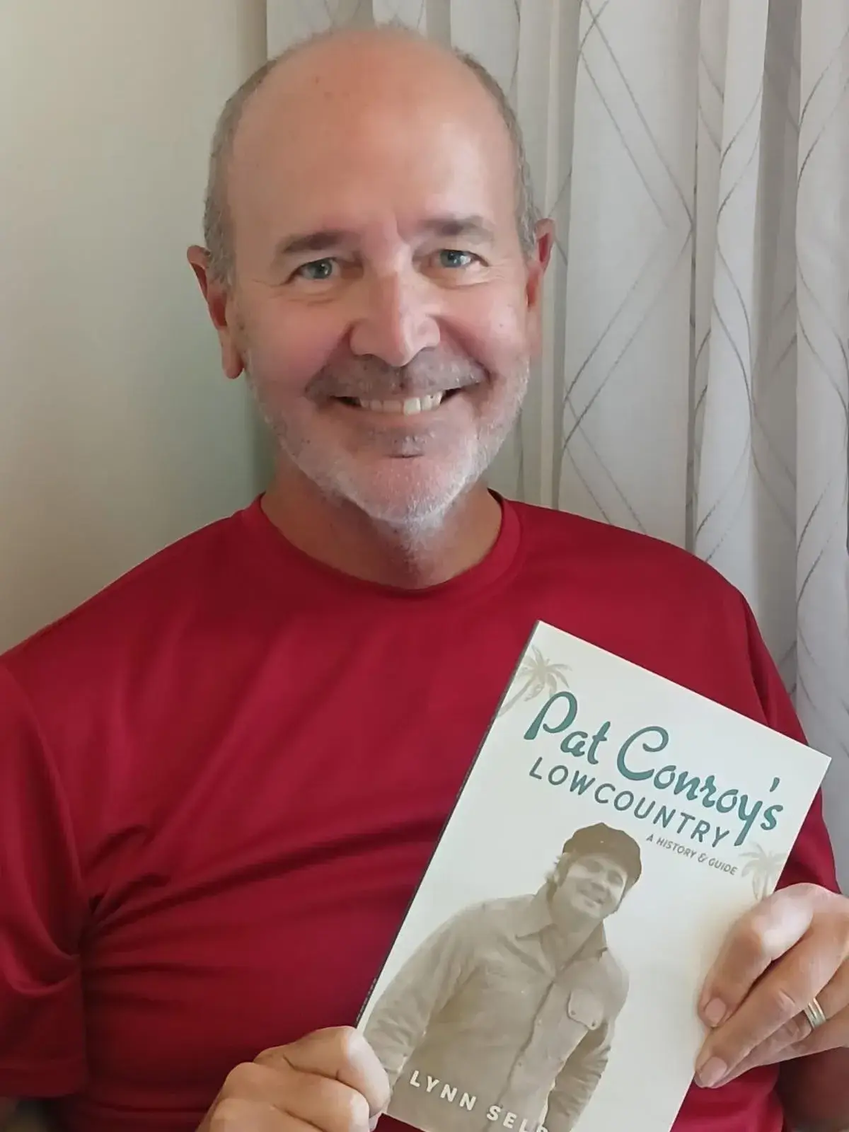 Lynn Seldon, smiling in a red T-shirt, holding up his book Pat Conroy's Lowcountry: A History and Guide