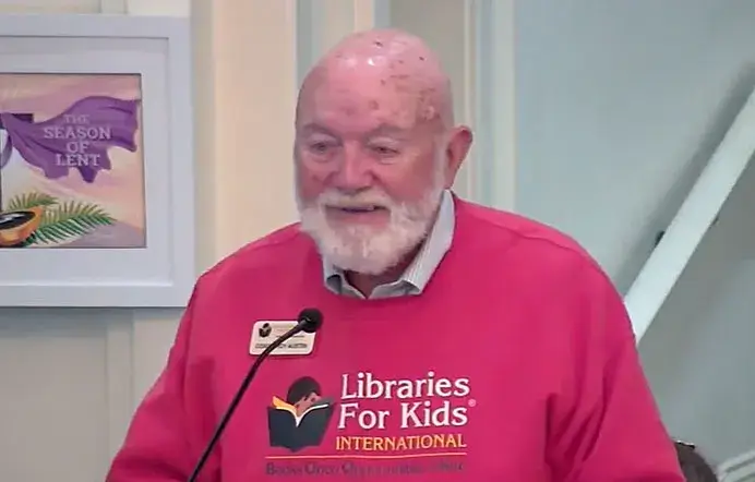 Roy Austin, an older man with white hair in a red Libraries For Kids sweater, speaking in a studio