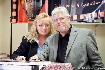 Jack Gannon, a man with white hair and a grey jacket, and Cyndi Williams-Barnier, a woman with fair hair, seated together at a table of books
