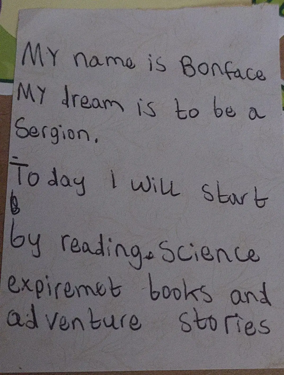 A student's handwritten note: My name is Bonface. My dream is to be a Sergion. Today I will start by reading Science experiment books and adventure stories