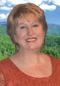 Barbara Bricker, smiling, in an orange top with green hills behind her