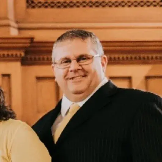 Paul Uhls, smiling, in a dark suit and tie in front of carved wood panelling