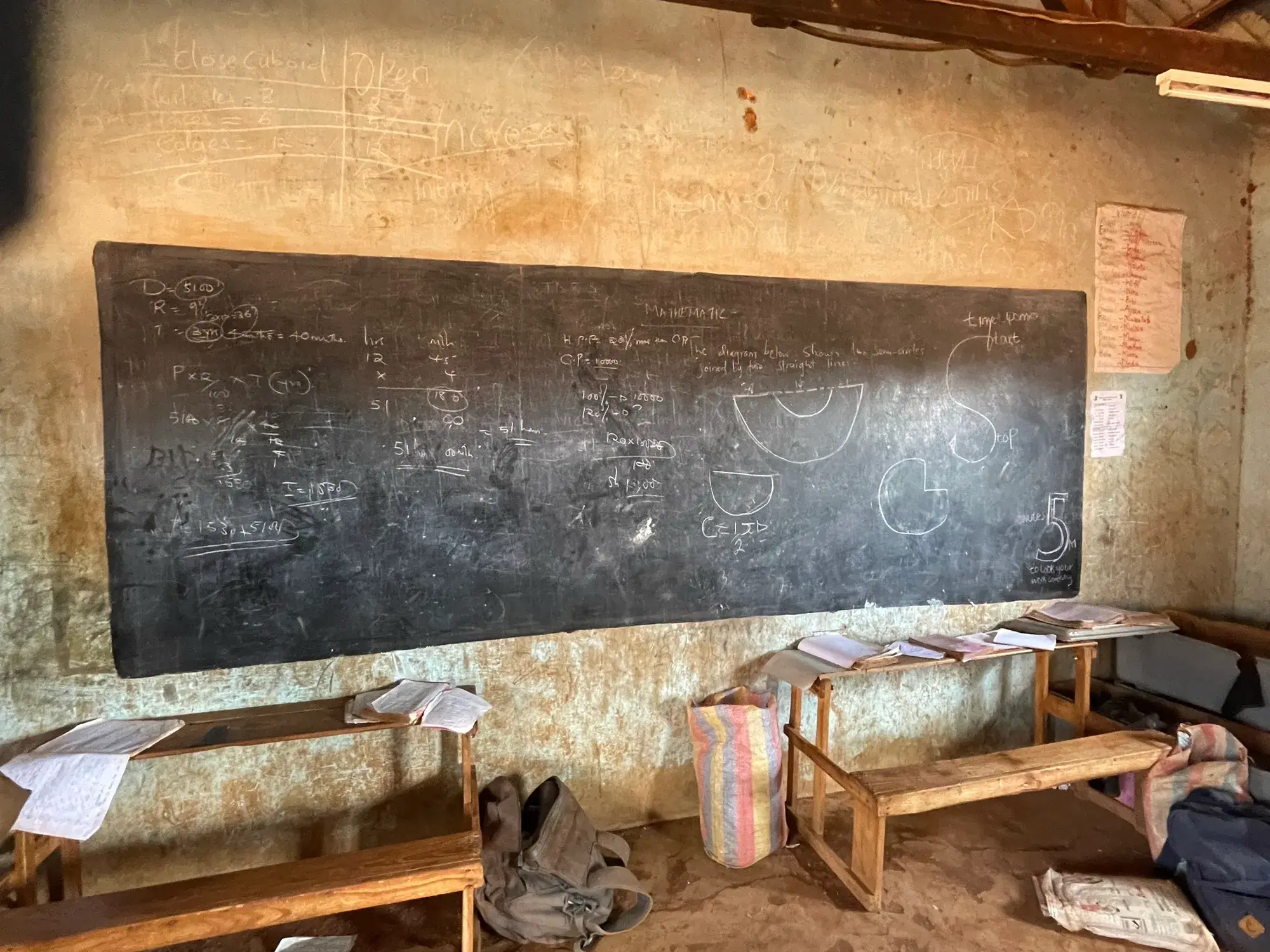 A worn chalkboard and wooden benches in a rural classroom
