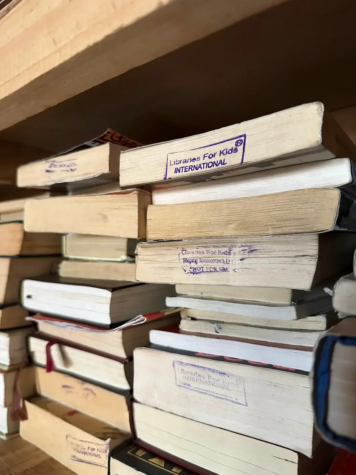 Stacks of books stamped Libraries For Kids International on a shelf