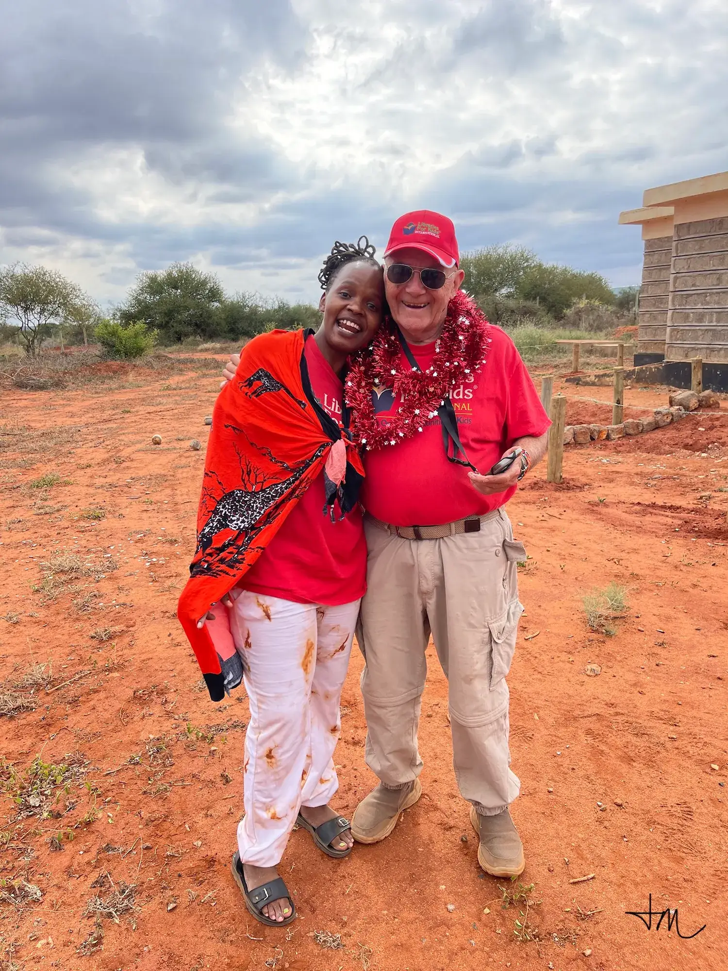 Coach Roy Austin wearing a beaded garland beside a woman in a red shuka at Kongoni