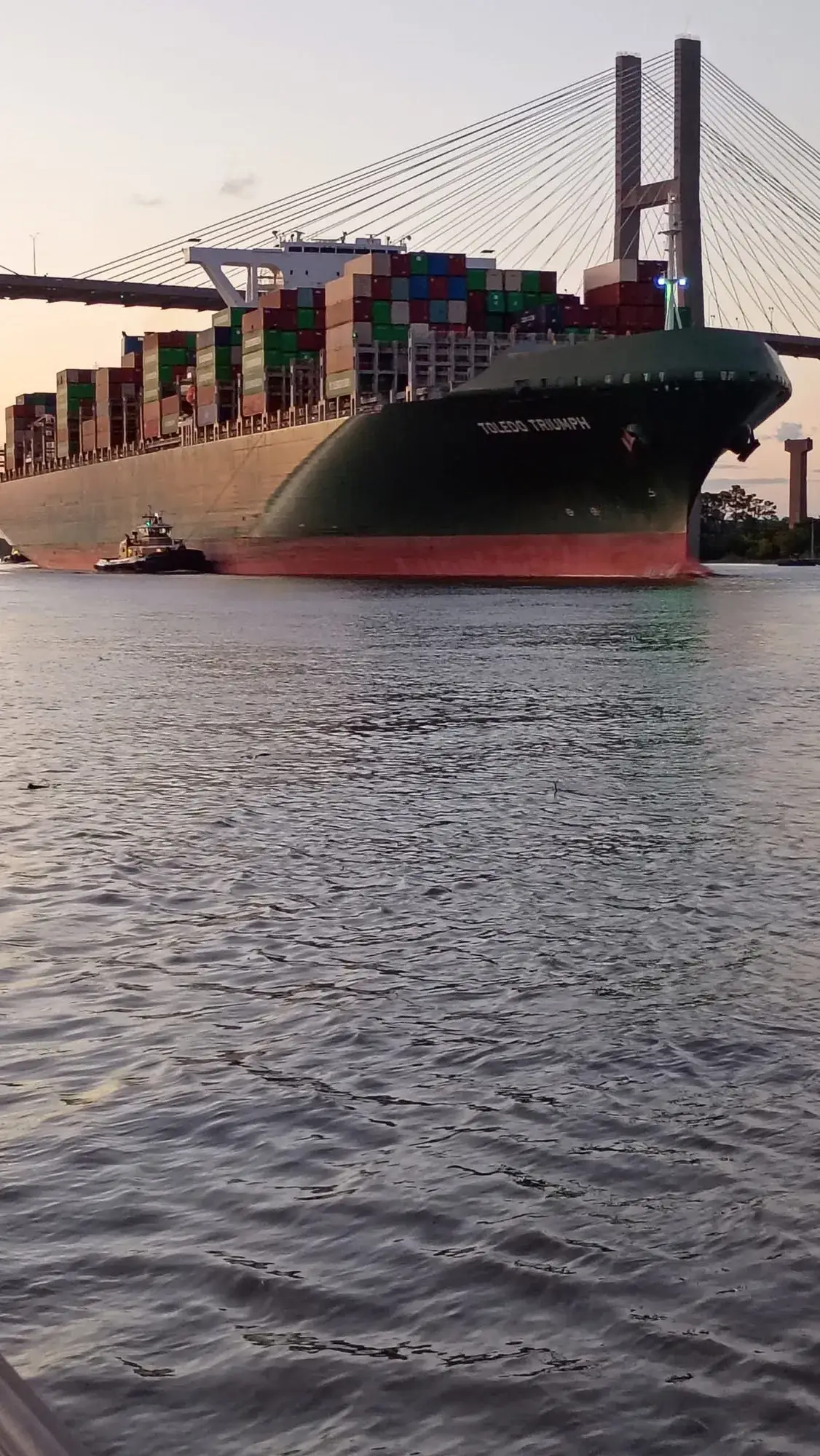 A container ship passing under a bridge at dusk