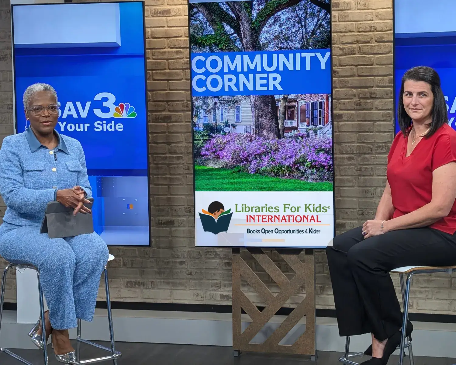 Laura Winkel seated across from a television host on the Community Corner set, a screen between them showing the Libraries For Kids International logo