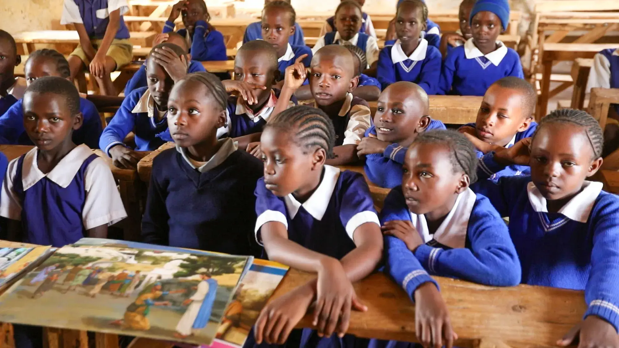 A class of pupils in blue uniforms leaning over picture books spread across their desks